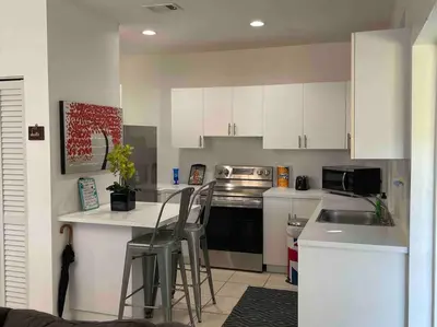 a kitchen with white cabinets and a counter with stools at ZION Miami Design District 2 Bedroom amongst the trees! in Miami