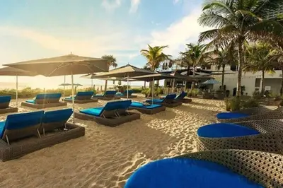 a beach with blue lounge chairs and umbrellas at Compact & Comfy, BeachWalk Studio for Small Groups in Hallandale Beach