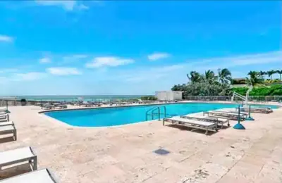 a swimming pool with benches and the ocean in the background at Entire Condo in Sunny Isles in Sunny Isles Beach