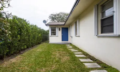 a white house with a blue door and a yard at Hidden Garden: A Serene Miami Escape in Cutler Bay