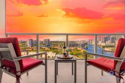 a balcony with two chairs and a table with a sunset at Modern Resort Retreat Steps from the Beach in Hallandale Beach