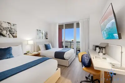 a hotel room with two beds and a desk and a window at Modern Resort Retreat Steps from the Beach in Hallandale Beach