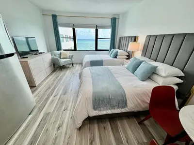 a bedroom with two beds and a chair and a television at Directly on the Beach with Pool & Ocean View in Miami Beach