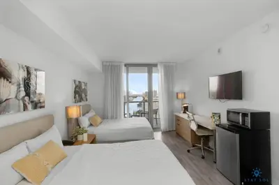 a hotel room with two beds and a desk at Resort Near Beach with Amazing Pool and Gym in Hallandale Beach