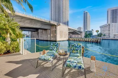 a patio with chairs and a table next to a body of water at Modern 2 BR - Beachwalk Resort - Pool - Gym in Hallandale Beach