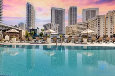a swimming pool with chairs and umbrellas in a city at Modern Condo - Amazing Pool - Gym - Balcony in Hallandale Beach