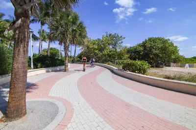 a person riding a bike on a brick path with palm trees at Ocean Drive Beach Fun, w/2 Queen Beds South Beach in Miami Beach