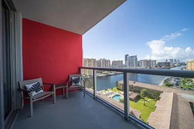 a balcony with two chairs and a red wall at Sunny Mornings & 2 Full Beds, BeachWalk Studio in Hallandale Beach