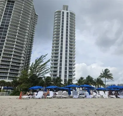 a beach with chairs and blue umbrellas and a tall building at Mare-1708 B in Aventura