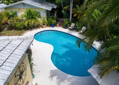 a swimming pool with a palm tree next to a house at Family Escape 2BR Main plus 1BR Cottage Heated Pool in Fort Lauderdale