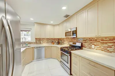 a kitchen with white cabinets and a stainless steel refrigerator at Tropical Oasis 6BR & 4BR Villa Heated Pool & Billiard Room in Hollywood