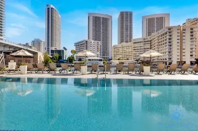 a swimming pool with chairs and umbrellas in a city at Spectacular Apartment Beachwalk Bliss Pool Gym in Hallandale Beach