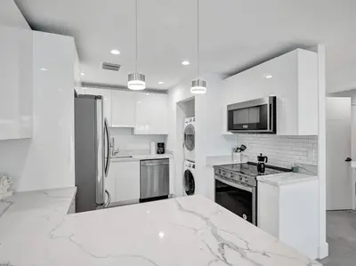a white kitchen with a refrigerator and a counter at Contemporary 2BR Home with Pool & BBQ Access in Fort Lauderdale