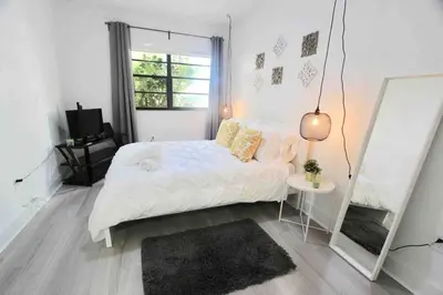 a white bedroom with a bed and a mirror at CHIC AND MODERN APARTMENT STEPS FROM THE BEACH in Miami Beach