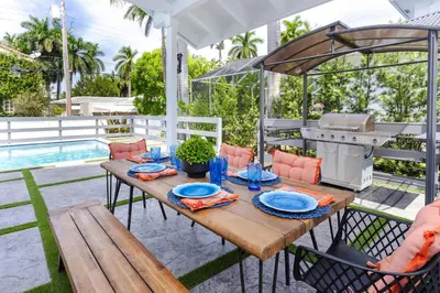 a wooden table with chairs and a grill on a patio at Luxury 5BR & 3BA Villa Walk to Hollywood Beach in Hollywood