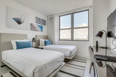 two beds in a room with a desk and a window at Walk to Hollywood Beach Upscale 16th-Floor Condo in Hollywood