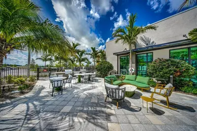 a patio with furniture and tables and palm trees at Hard Rock Stadium Home Base! Luxe Condo with Pool in Joe Robbie Stadium Heliport