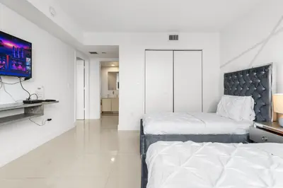 a white bedroom with two beds and a tv at Spacious Luxury Apartment at Beachwalk Resort with Ocean Views and Private Foyer in Hallandale Beach
