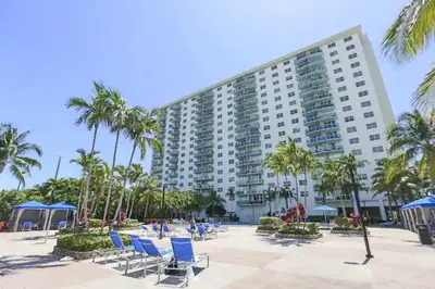 a large building with blue chairs and palm trees at Beautiful and big Apartment by the beach in Sunny Isles Beach