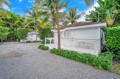 a white house with a garage next to palm trees at Renovated Grove Bungalow -near Coconut Grove in Miami