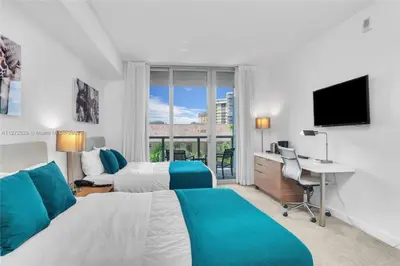 a hotel room with two beds and a desk and a television at Beautiful 2BR Balcony Pool Near Beach & Fun in Hallandale Beach
