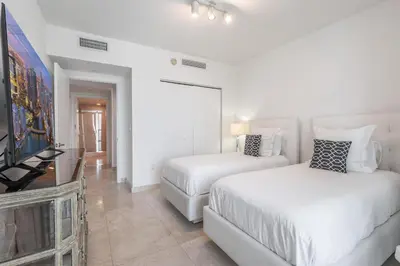 a white bedroom with two beds and a flat screen tv at ICON Brickell Miami- 2 bedroom Condo with City and water views! in Miami