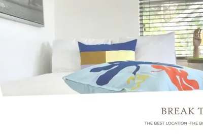a bed with white sheets and colorful pillows on it at B01 Minutes from the beach Studio Midtown Wynwood in Miami