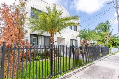 a fence in front of a house with a palm tree at Magical bright Apt 5min walking Design District apt 5 in Miami