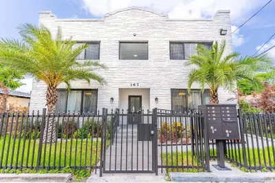 a white house with palm trees in front of a fence at Quiet Bright Apt 5min walking to Design District apt 6 in Miami