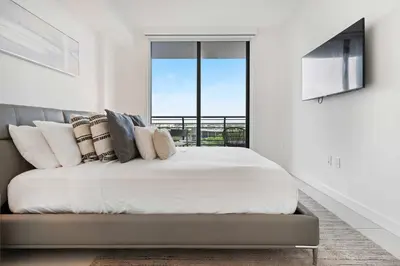 a white bedroom with a bed with a large window at La Central- CityPlace Doral and across from a Park in Miami