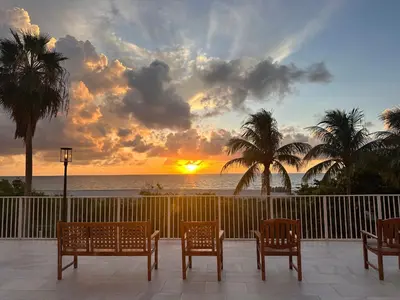 a sunset over the ocean with chairs and palm trees at Luxury Ocean Front Condo on Millionaires Row in Miami Beach