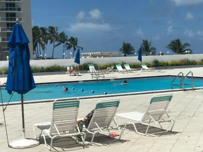 a swimming pool with chairs and a blue umbrella at Luxury Ocean Front Condo on Millionaires Row in Miami Beach
