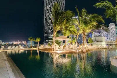a pool with palm trees and a city at night at Lux 2BR Natiivo Condo With Pool, Spa and Gym Access in Miami