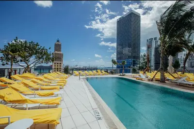 a swimming pool with yellow lounge chairs and a building at 49th Floor Sleek Condo Cozy Pool, Gym and Spa Stay in Miami