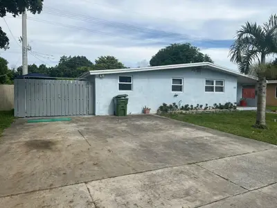 a white house with a fence and a driveway at Relaxing Studio Getaway w BBQ, Patio and Parking in Pembroke Pines