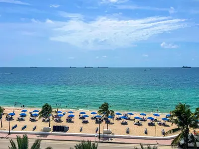 a beach with blue and white umbrellas and the ocean at 2BR W Residence FLL, OCEAN VIEWS, Infinity pool, hot tub, large balcony, easy amentiy access in Fort Lauderdale