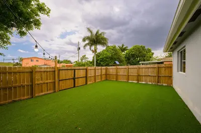 a backyard with a wooden fence and green lawn at House Genesis in Homestead