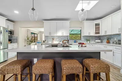 a kitchen with white cabinets and a island with bar stools at 3-Bedroom Villa with Heated Pool and Tropical Yard in Hollywood Lakes in Hollywood