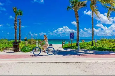 a woman riding a bike on a sidewalk near the beach at Castle 732 Ocean View with pool, tennis, beach access, FREE parking in Miami Beach