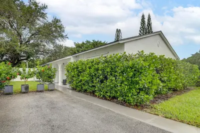 a white house with a large bush in front of it at The Peacock Bungalow Near Fort Lauderdale Beach! in Fort Lauderdale