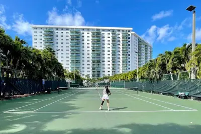 a woman is playing tennis on a tennis court at Spacious 3 BR plus 1 office and 2 BA with Free parking Just in front beach in Sunny Isles Beach