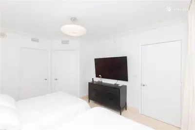 a white bedroom with two beds and a flat screen tv at Elegant Resort - Beautiful Views in Hallandale Beach