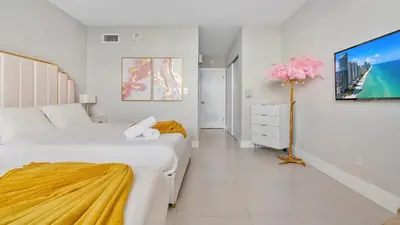 a white bedroom with two beds and a tv at Absolute Beach Bliss, Chic & Expansive Retreat in Sunny Isles Beach