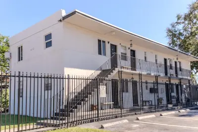 a white building with a fence in front of it at Queens Cozy Condo Near Downtown Airport in Miami