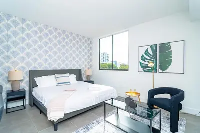a bedroom with a bed and a chair and a glass table at Chic Spacious Studio Miami Stay Near Marlins Park & Brickell in Miami