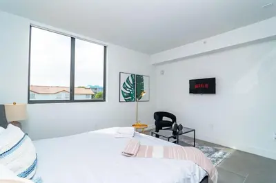 a white room with two beds and a chair at Chic Spacious Studio Miami Stay Near Marlins Park & Brickell in Miami