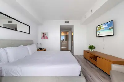 a white bedroom with a large bed and a television at Deluxe Apartment with Balcony Gym & Pool in Hallandale Beach