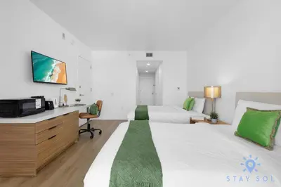 a bedroom with a bed and a desk with a tv at Modern 2BR 2BA Oasis & pool in Hallandale Beach