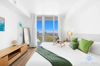 a white bedroom with a large bed with green pillows at Urban Apartment Balcony & Pool in Hallandale Beach