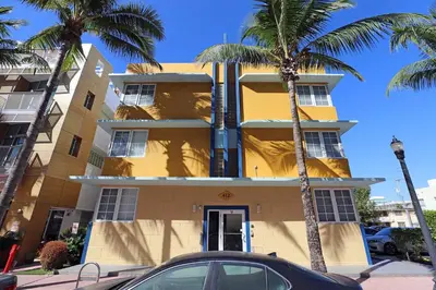 a yellow building with palm trees in front of it at Art Deco Suite Steps from Beach in South of Fifth in Miami Beach